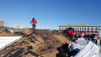 Roofing crew tearing off a roof with wood damage