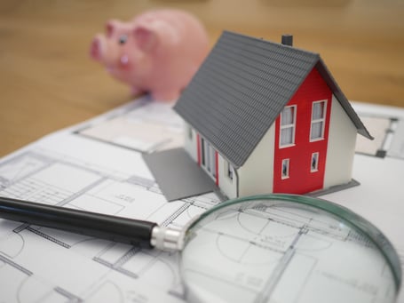 model home, piggy bank , magnify glass, blueprints sitting on a table, searching for contractors