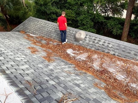 roofer inspecting an asphalt shingle roof with leaves and debris in a valley