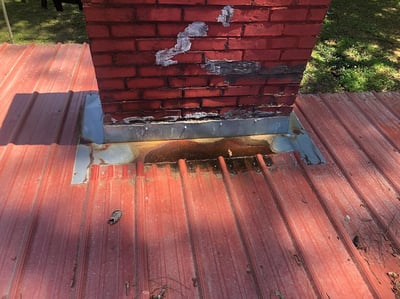 rusted flashing at a brick chimney coming through a metal roof 