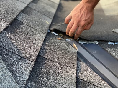 hand lifting loose shingles in valley during a roof inspection