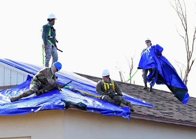 roofers installing a tarp on a roof