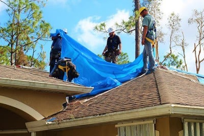 Roofing crew installing a tarp on a roof