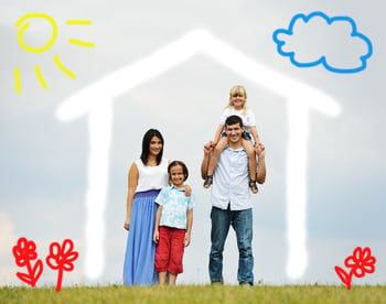 A young family of four standing in front of a cartoon home drawn on a backdrop, image of flowers, clouds, and the sun too.