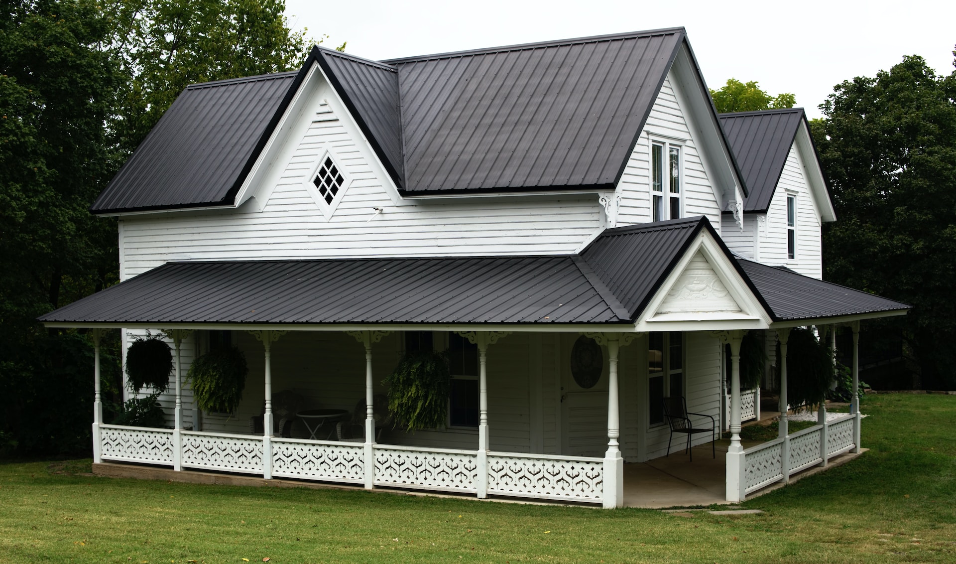 White house with wrap around porch and black metal roofing
