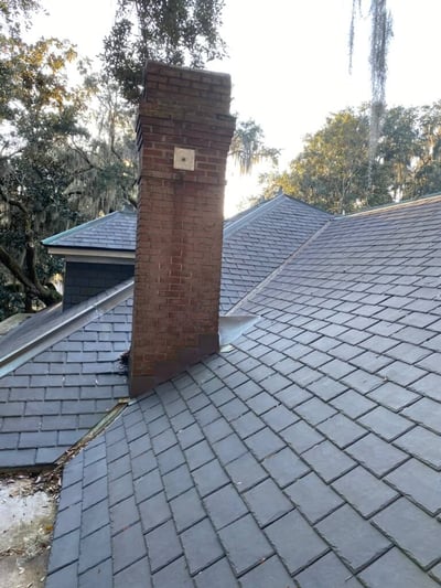 brick chimney on a synthetic slate roof with copper ridge caps and valley