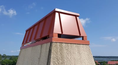 red chimney cap with standing seam windscreen on stucco chase