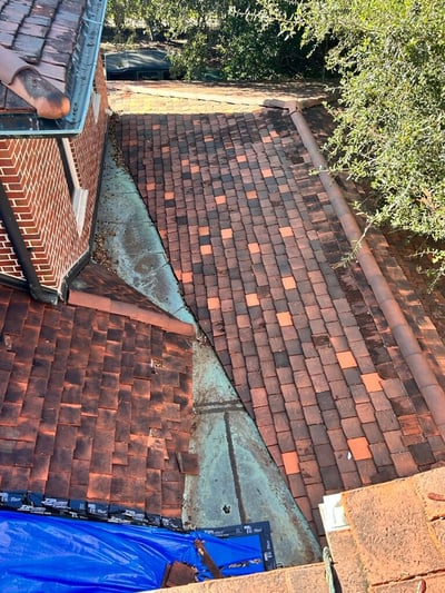 Flat clay tiles on a roof with copper valleys that is leaking with a tarp