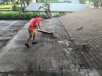 roofer on flat roofing brooming off the debris