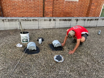 roofer doing a repair to vents on a hot tar roof with rocks