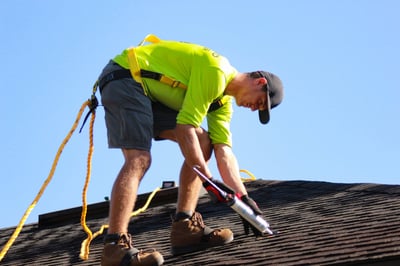 A roofer sealing nail pops on a shingle roof with caulk