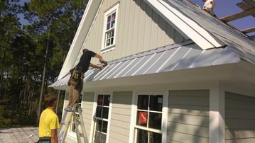 roofers installing a screw-down metal roof off a ladder