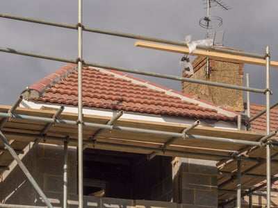 scaffolding surrounding a steep hip roof that is getting Spanish tiles installed