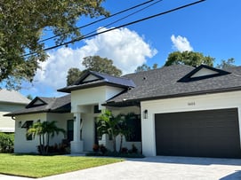 stucco home with dark shingle roof with a metal accent over front entrance