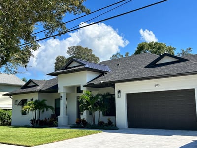 stucco home with dark shingle roof with a metal accent over front entrance