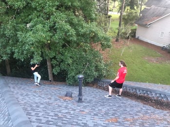 2 roofers looking at trees overgrowing on a brand-new shingle roof