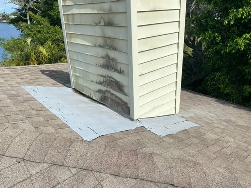 chimney coming through a roof with a shoddy repair on the shingles