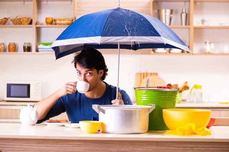 man drinking coffee inside with an umbrella, pots, and pans catching roof leaks