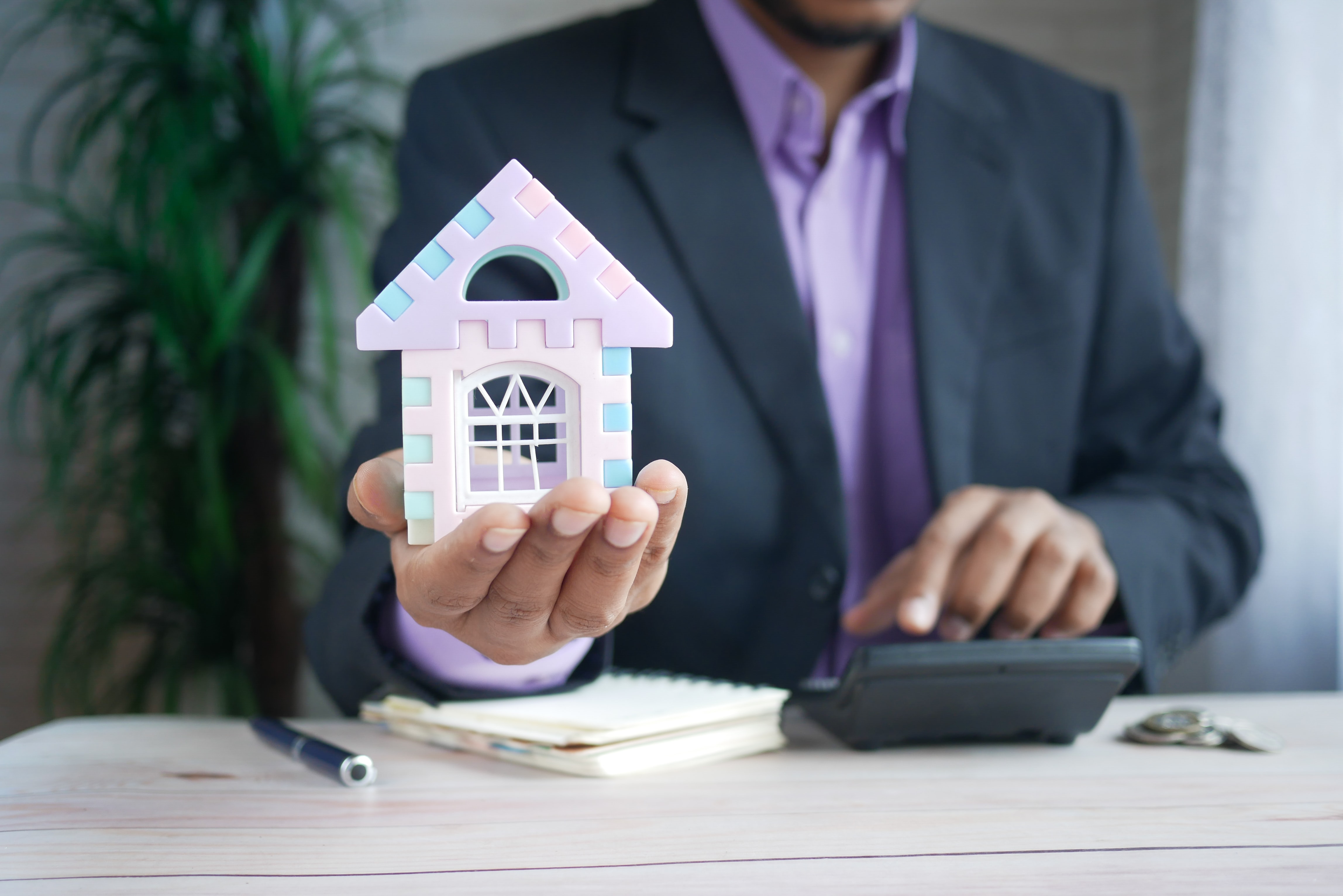 a man sitting at a desk holding a house and using a calculator