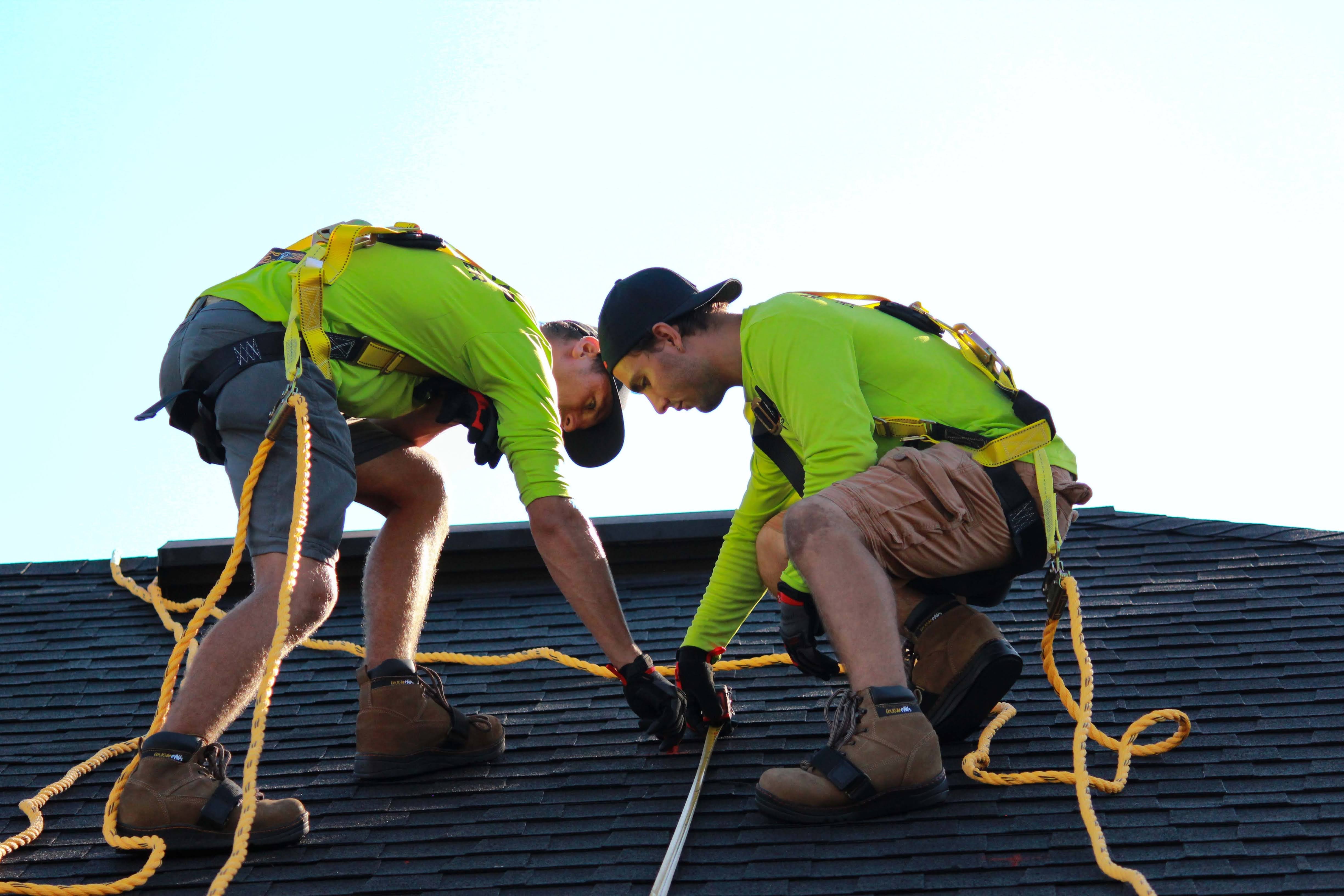 two roofers wearing safety harnesses on roof