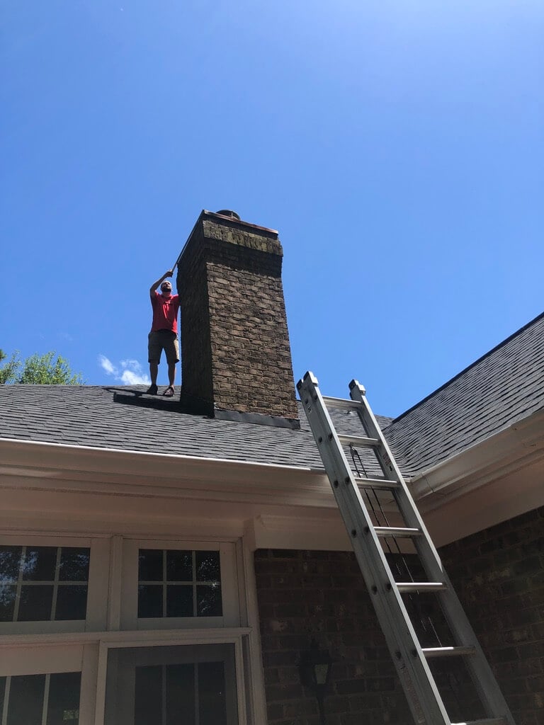 roofer inspecting a chimney cap on a brick chimney